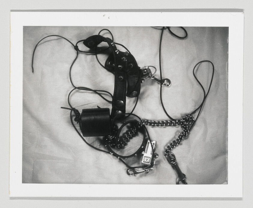 Tangled leather straps, metal chains, and clips laid in a messy pile on light fabric.