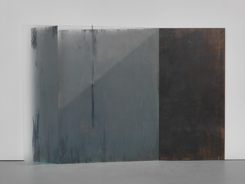 Two large vertical panels lean against a white wall, one translucent gray-blue with drips and one dark brown.