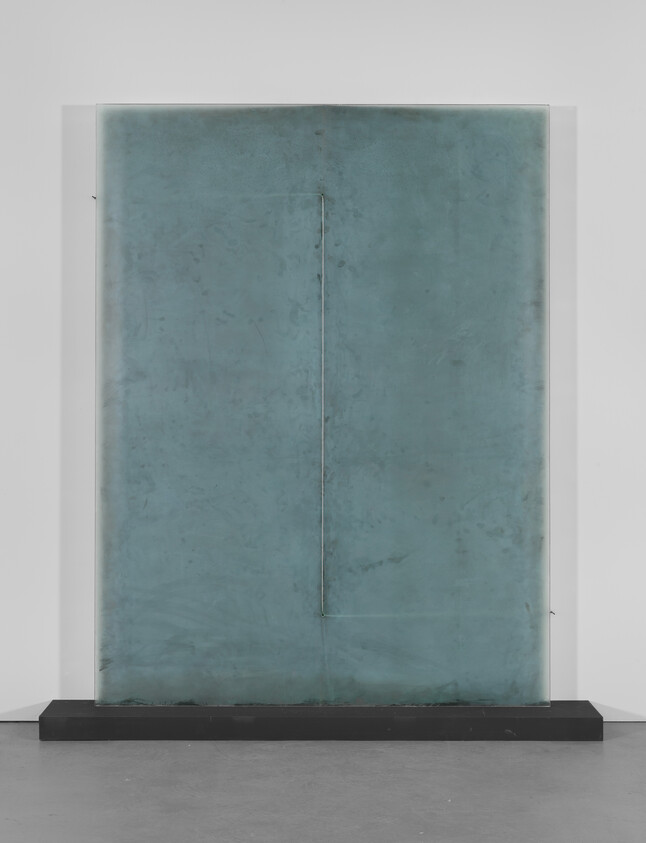 A large rectangular teal glass panel with faint seams stands on a low black base.