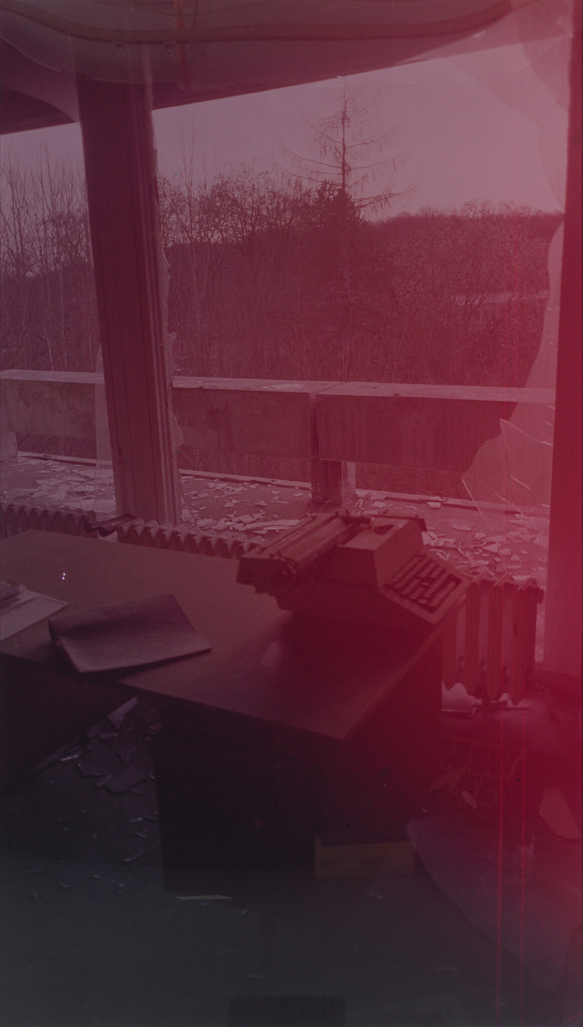 An old typewriter sits on a desk in a room with broken windows and scattered debris.