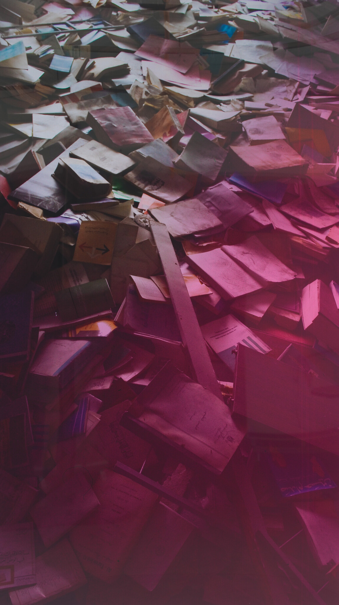 A large pile of worn books and papers scattered across the floor under pink light.