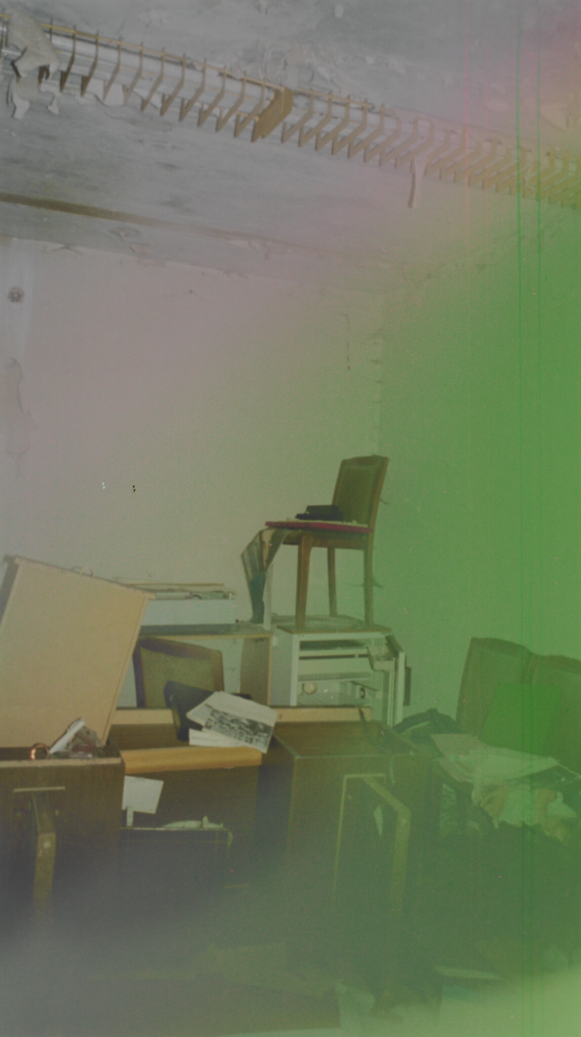 Cluttered room with stacked furniture and a chair balanced on top of cabinets amid scattered papers.