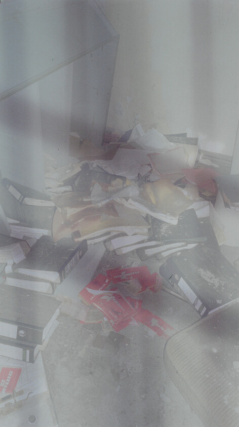 Scattered books, folders, and papers strewn across a dusty floor beside a cabinet.