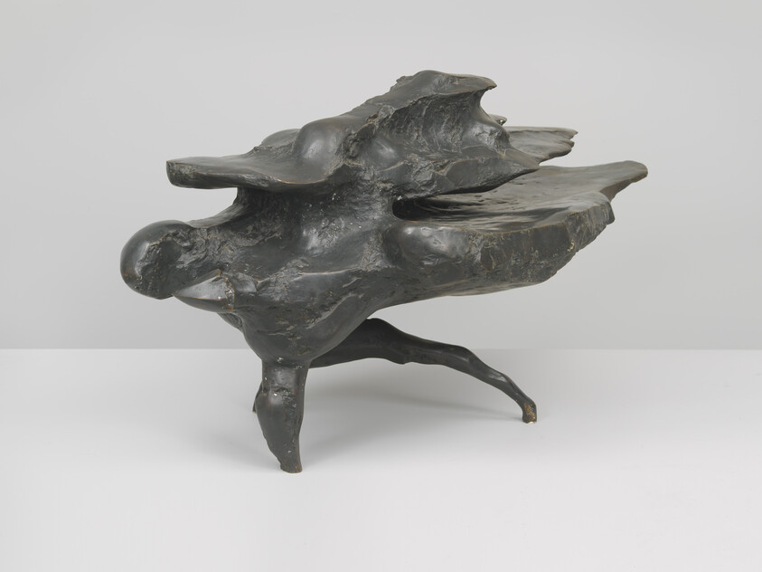 A dark bronze abstract sculpture with flowing organic shapes balancing on three short legs.