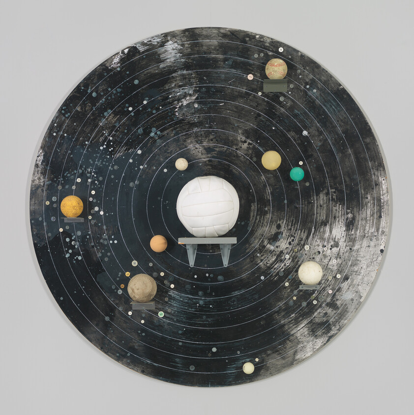 Round black board with concentric rings showing planets made from sports balls orbiting a central volleyball.