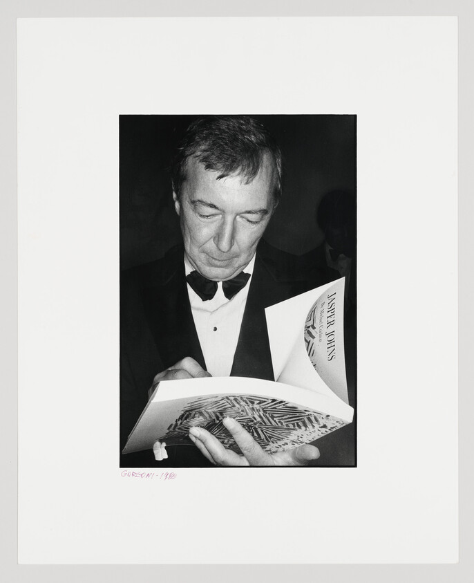A man in a tuxedo studies and signs a book about Jasper Johns.