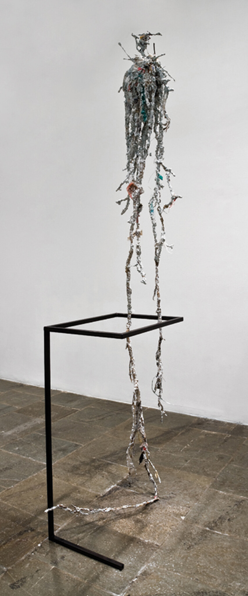 Tall hanging sculpture with tangled metallic strips dangling from a simple black metal stand.