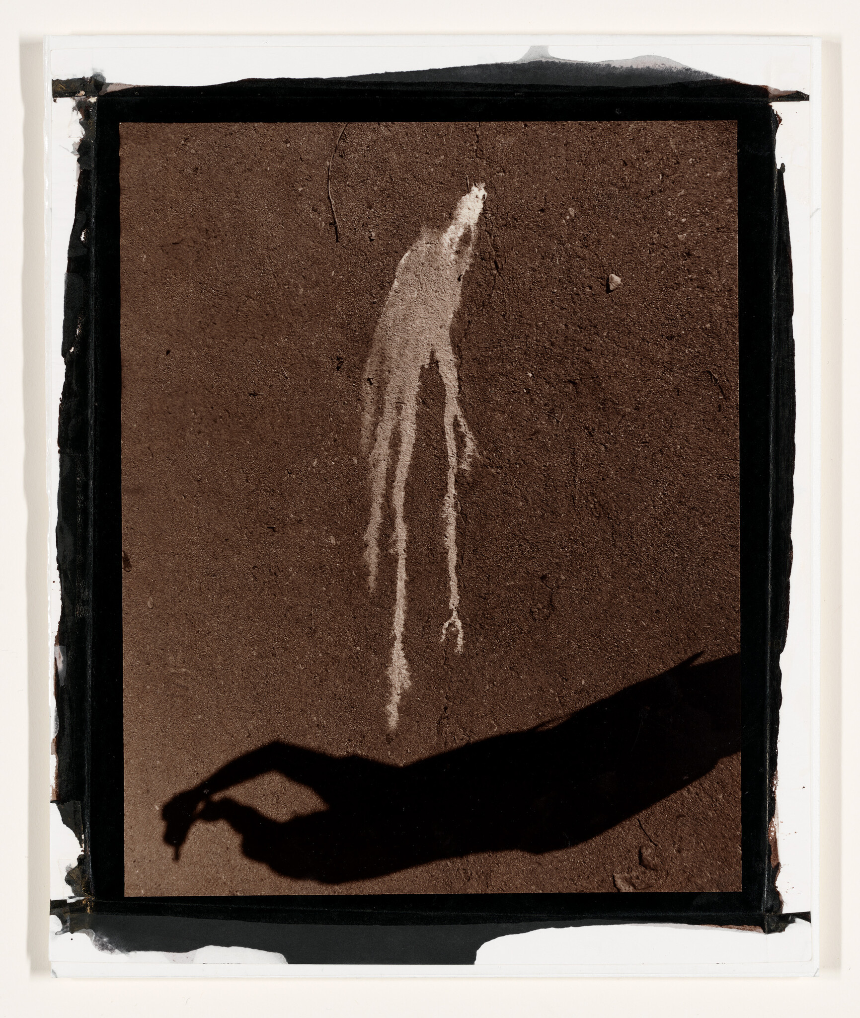 Long shadow of a hand and arm reaches toward white paint drips on a textured ground.