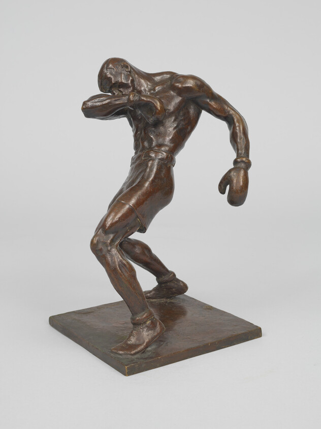 Bronze sculpture of a boxer recoiling and shielding his face with one gloved hand.