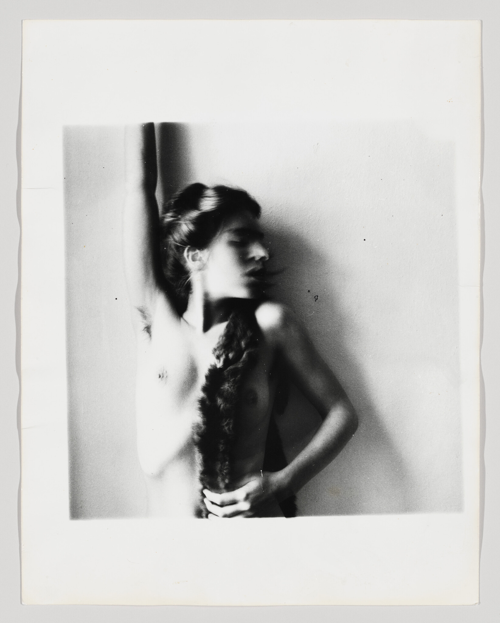 A nude woman looks to the right as her bent right arm touches her braid