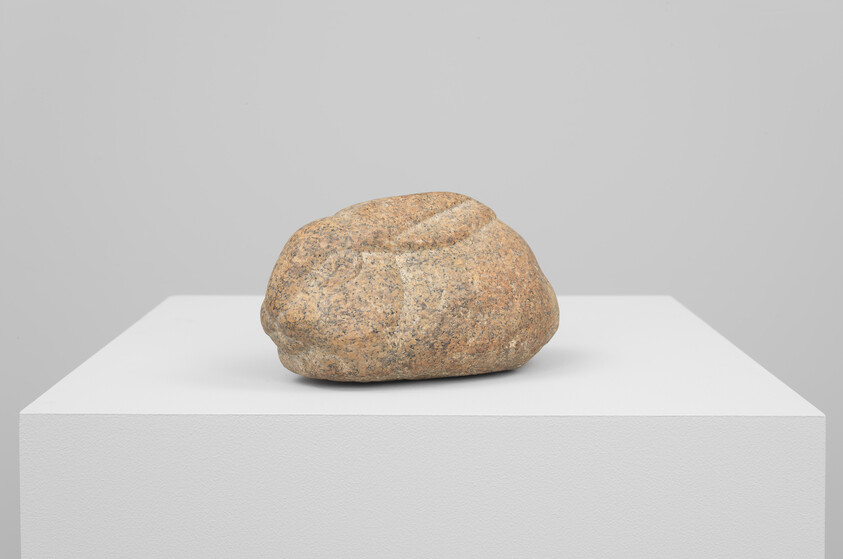 A rounded brown rock with a shallow depression sits on a white display pedestal.