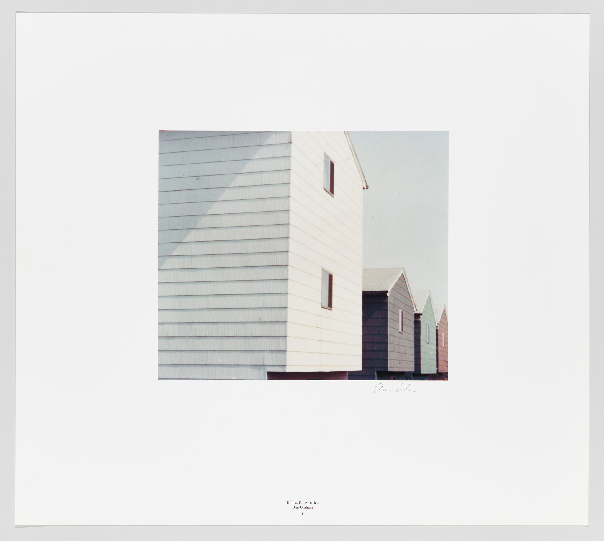 A photograph of a series of white, wooden-sided buildings with a minimalist design, receding in perspective. The closest building is larger and more detailed, with visible windows, while the others appear progressively smaller. The image includes a caption at the bottom that reads "Houses for America, Dan Graham" with a signature on the right. The photo is mounted on a white background with a wide border.