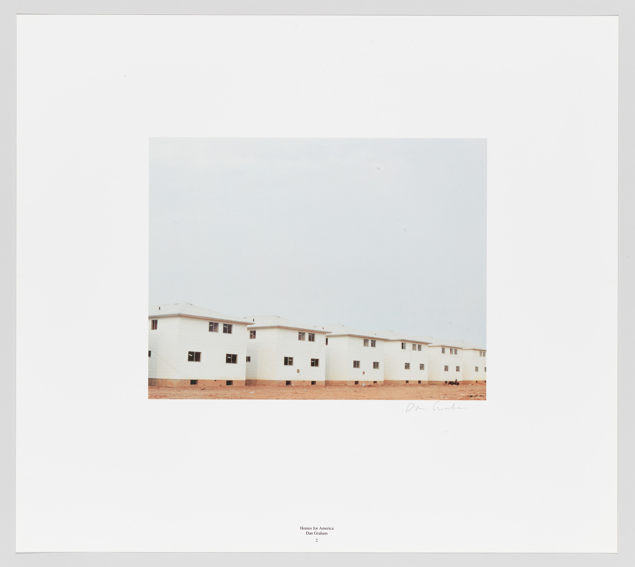 A photograph of a row of identical white houses with flat roofs under a pale sky, centered within a white border that contains a title and signature at the bottom.
