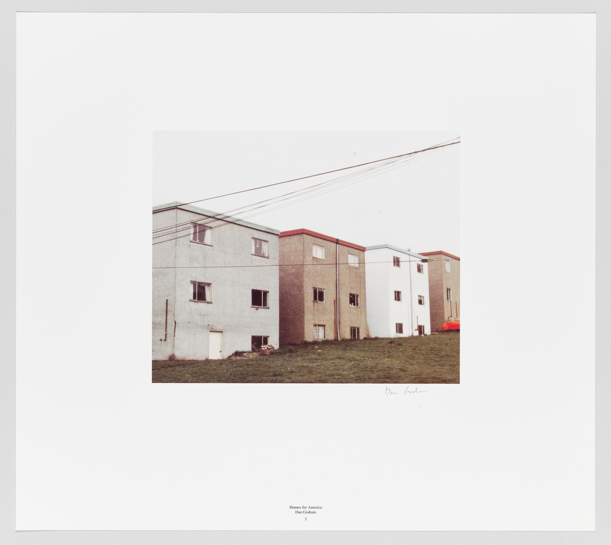 A photograph of a plain, two-story residential building with a flat roof and several visible windows. The building is set against a clear sky with a grassy foreground. There are power lines crossing in front of the building. The image includes a caption at the bottom and a signature on the right, suggesting it is an artwork or a print.