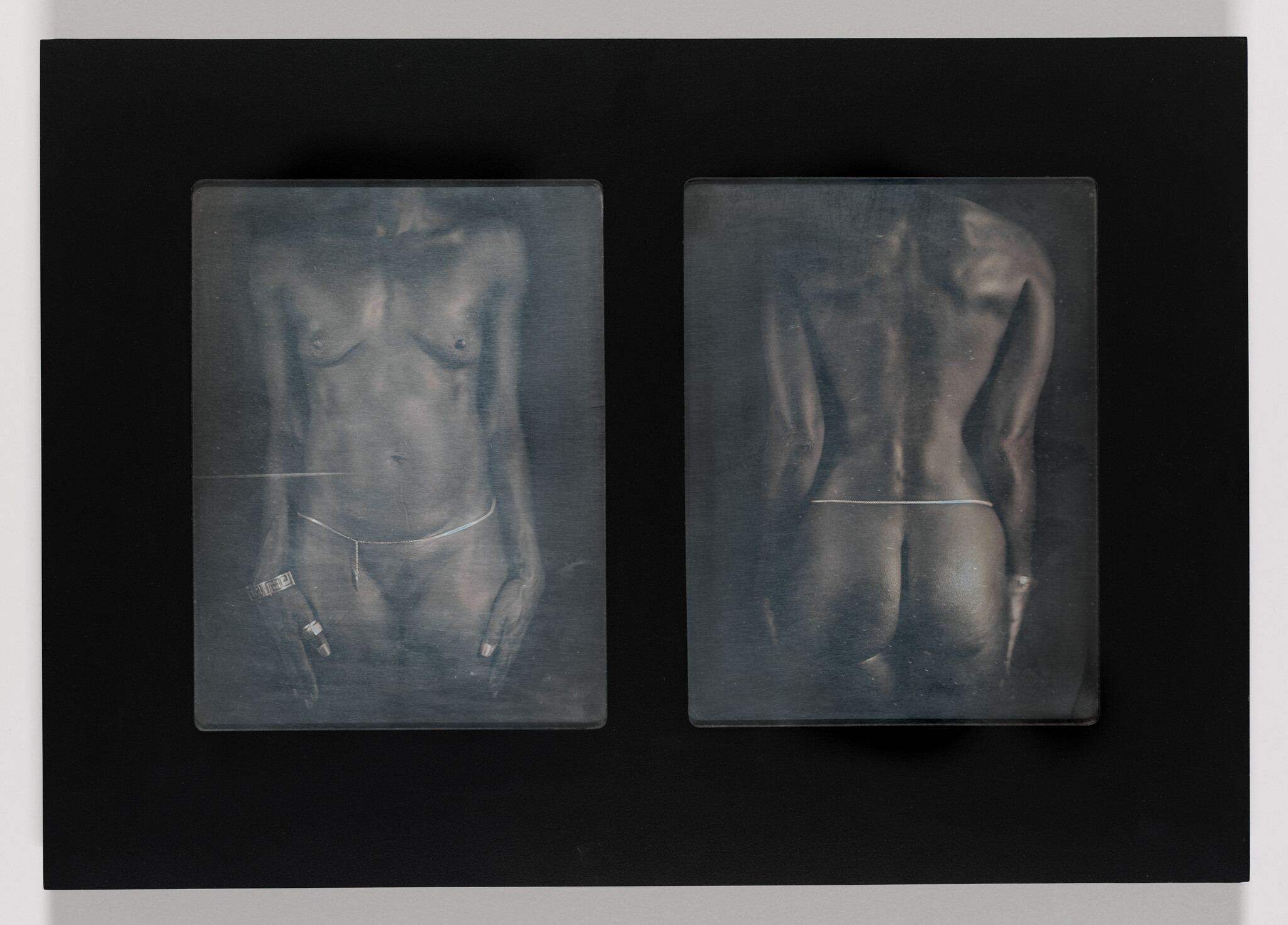 Two monochromatic, translucent panels depicting the front and back of a human torso, displayed against a black background. The images resemble X-ray scans, showing skeletal and muscular structures with a faint outline of undergarments.