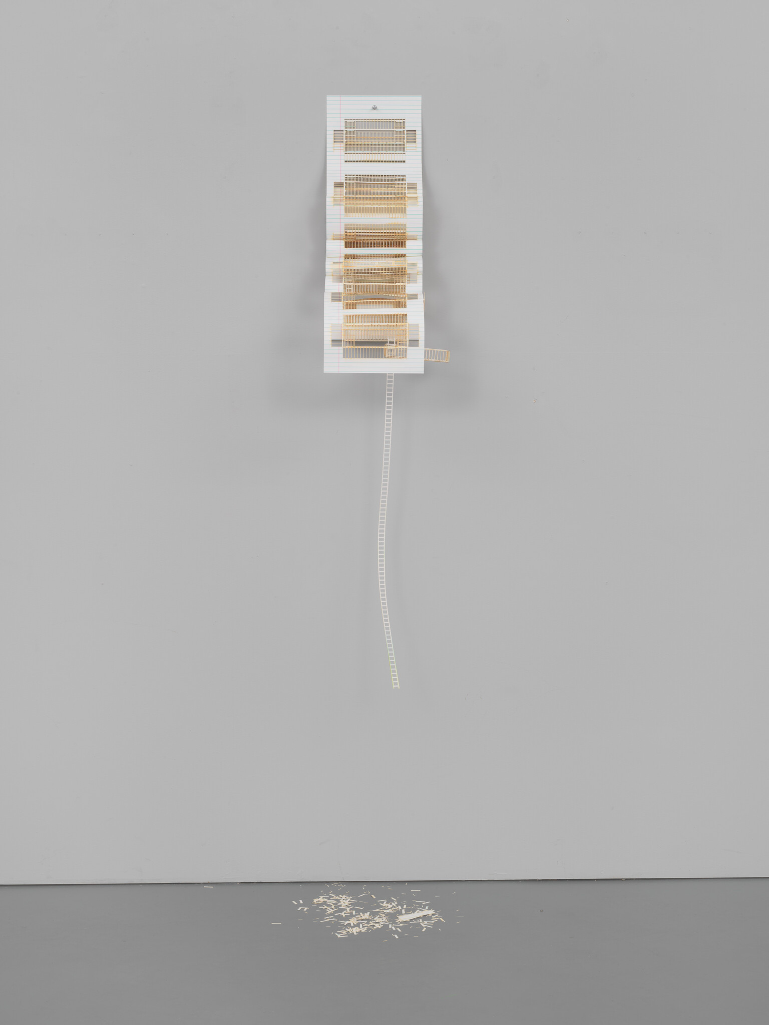 A small white architectural model hangs high on a gray wall with a dangling ladder and wood shavings below.