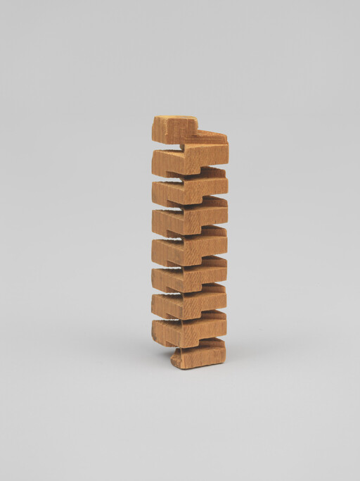 A tall tower of interlocking wooden blocks stacked vertically on a plain gray background.