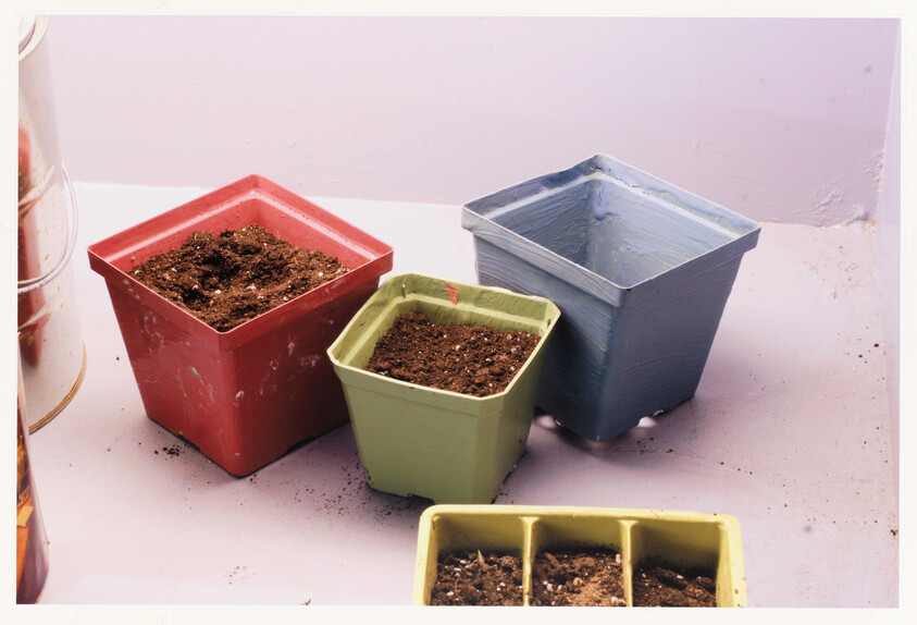 Three empty square plant pots and a small seed tray sit on a surface with soil.