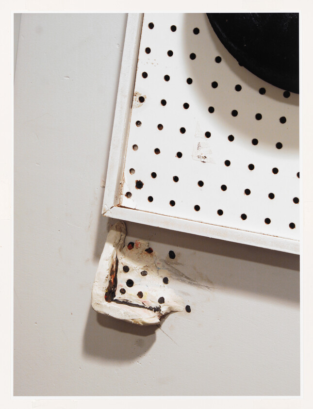 A white pegboard mounted on a wall with a damaged corner and melted plastic patch.