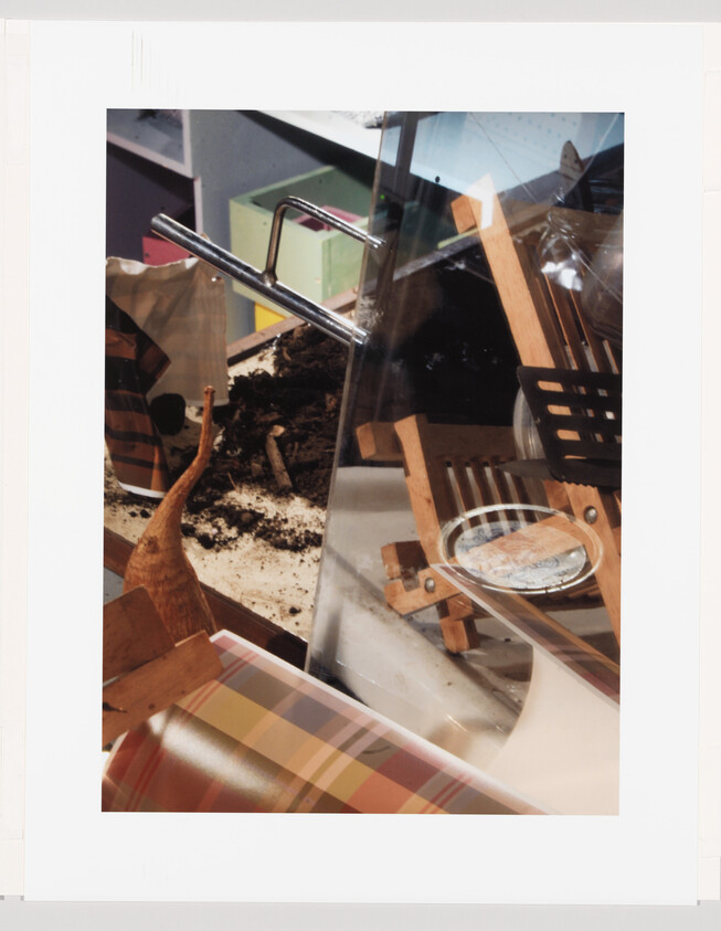 Wheelbarrow handles rest over spilled soil beside a wooden folding chair and plaid fabric.