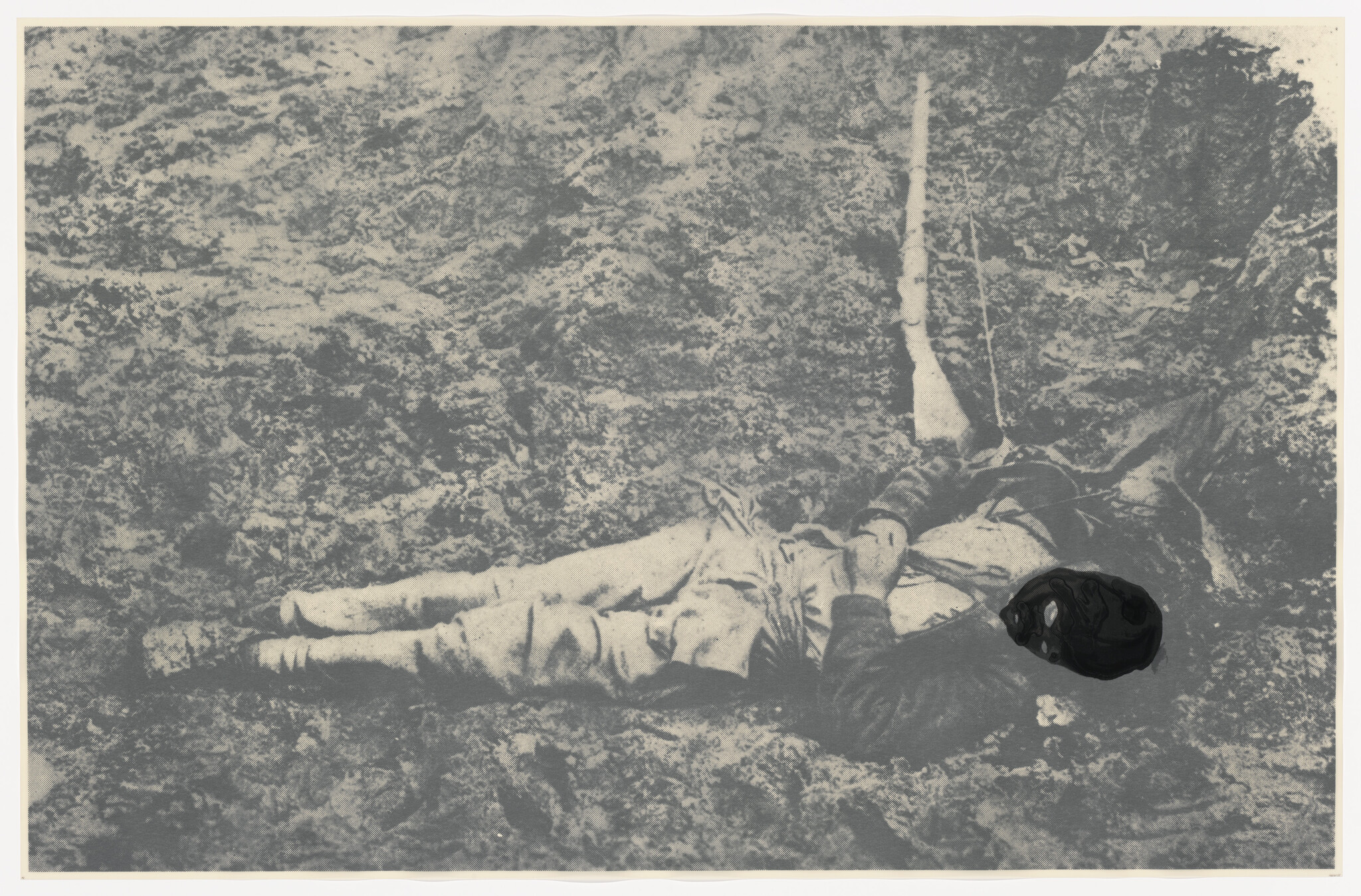 A person in uniform lies on the ground beside an upright rifle, with the head obscured by a dark blot.