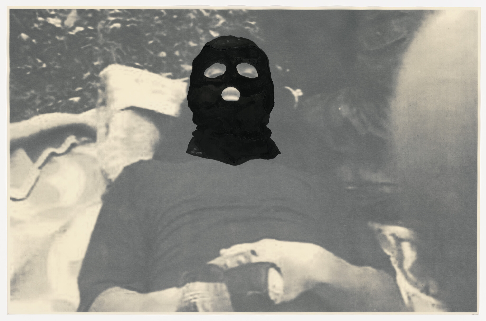 A person lies down wearing a black balaclava mask with visible eye and mouth openings.