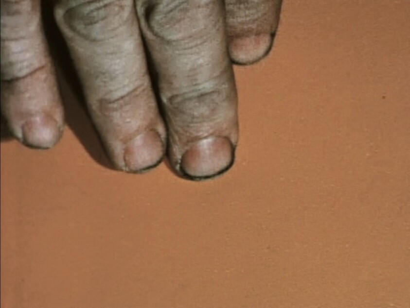 Three fingers with dirty nails and rough skin rest on a plain orange surface.