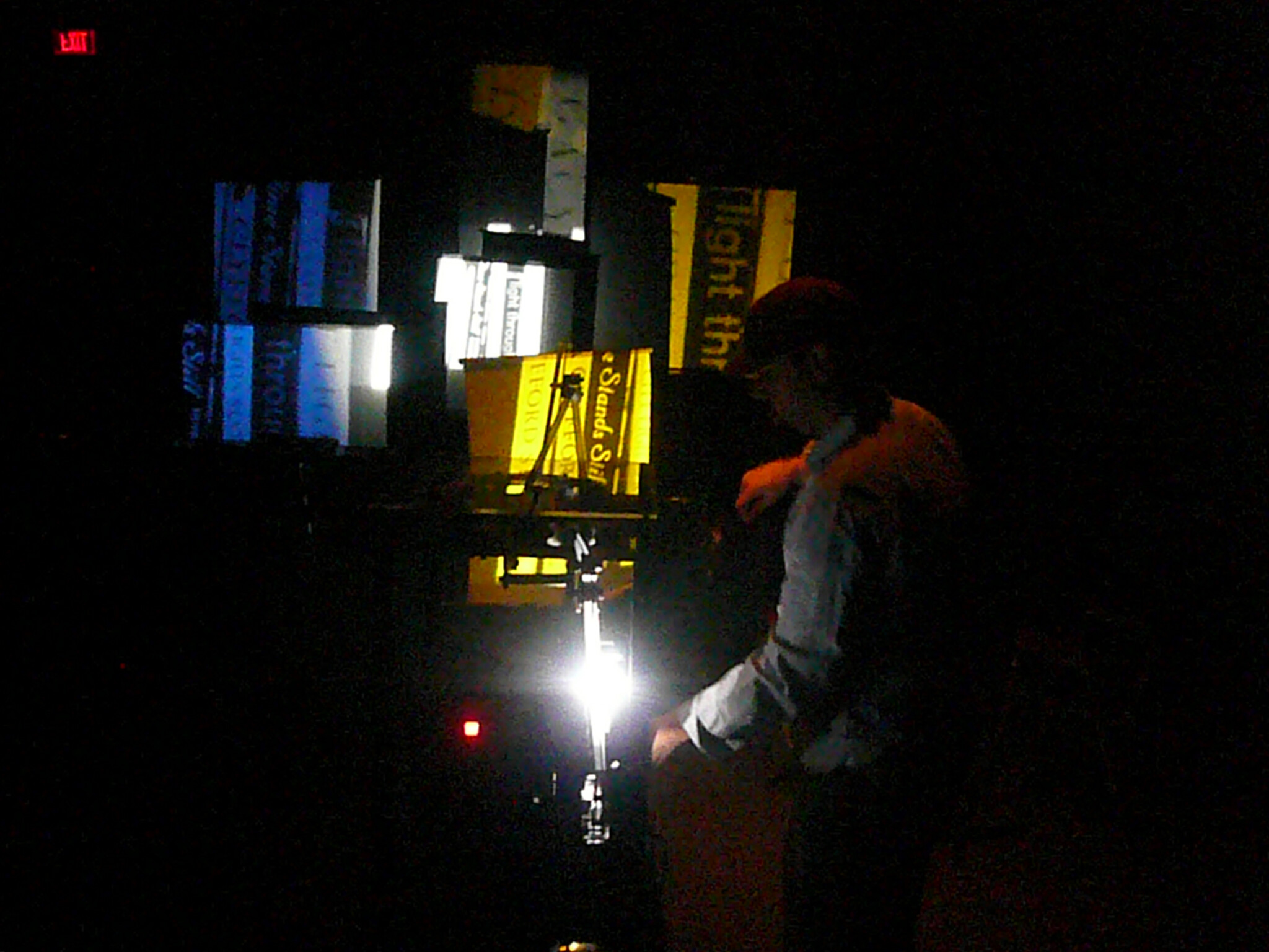Person adjusting equipment in a dark room with illuminated text projections on the wall.