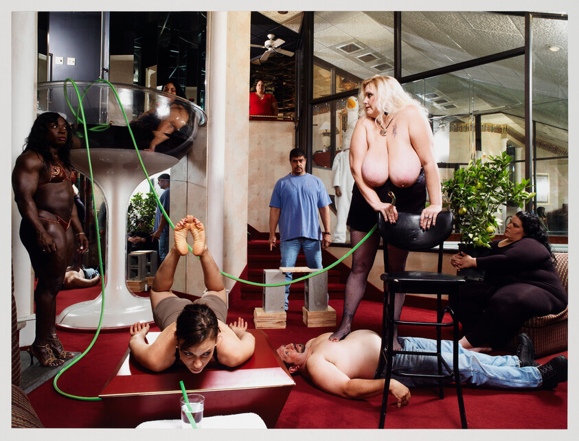 A woman stands on a stool while a man lies on the floor connected by a green tube.