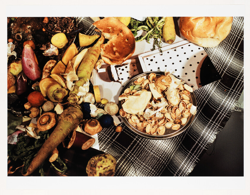 Bowl of pistachio shells and assorted food scraps, peels, and bread on a checkered cloth.