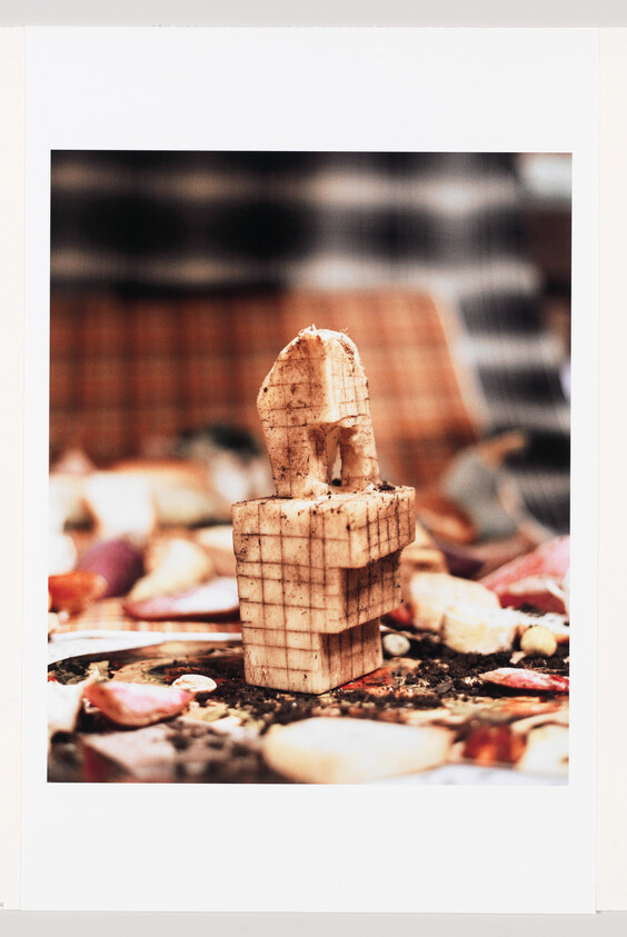 A small carved wooden tower with grid marks stands among flower petals and dirt.