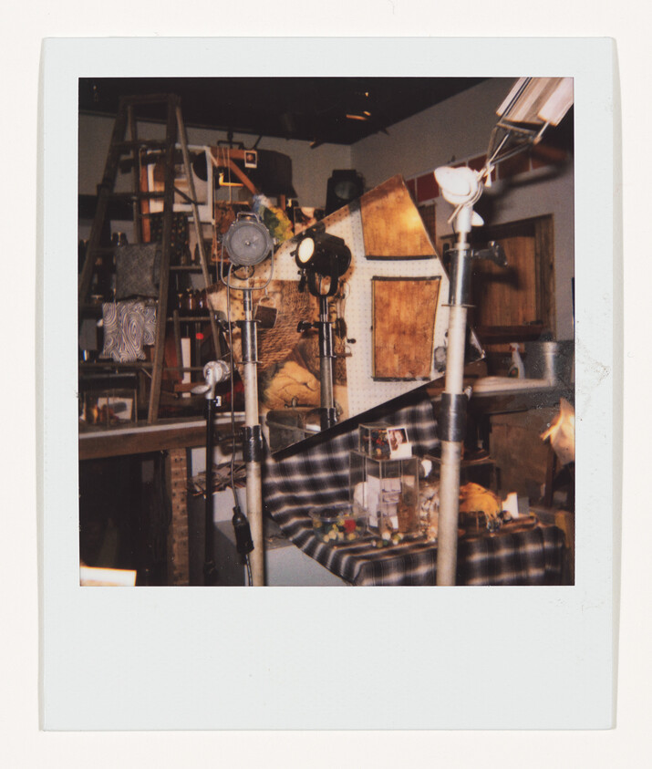 Three studio lights on stands illuminate a cluttered workshop table covered with tools and props.