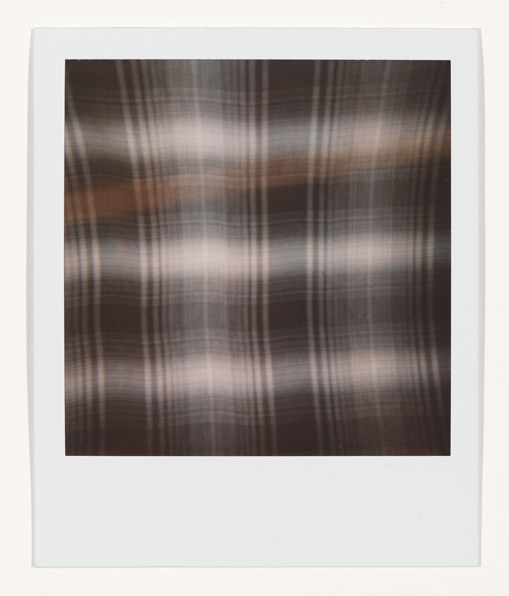 Blurred brown and gray plaid pattern inside a white polaroid-style frame.