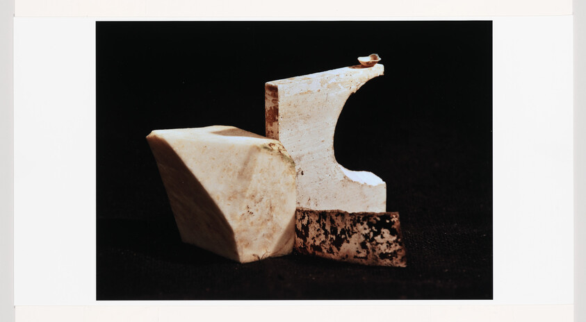 Three white stone sculpture pieces arranged on a black surface, one with a curved cutout and chipped base.