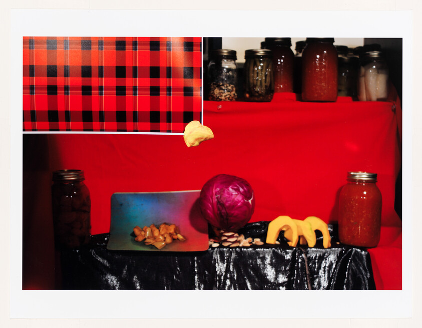 A kitchen scene with jars, a purple cabbage, sliced squash, garlic, and a red plaid cloth.