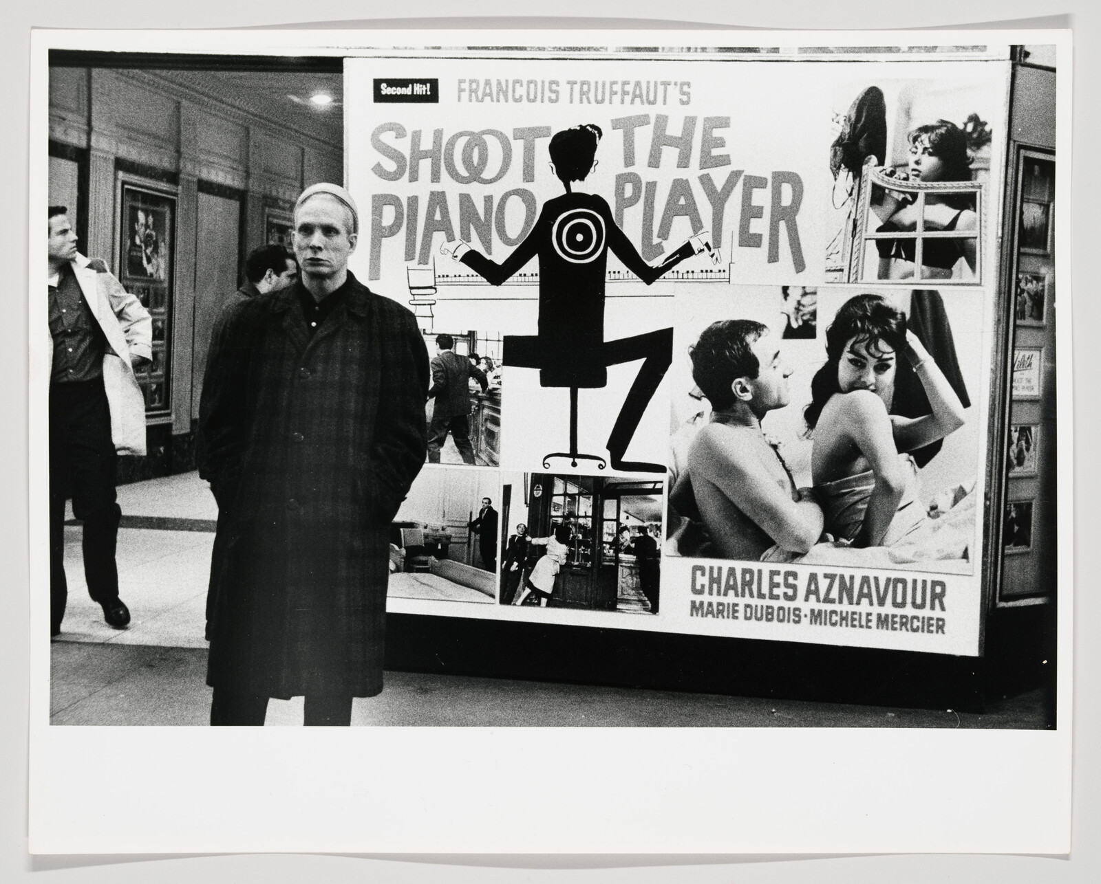 A man stands in front of a large "Shoot the Piano Player" movie poster in a hallway.