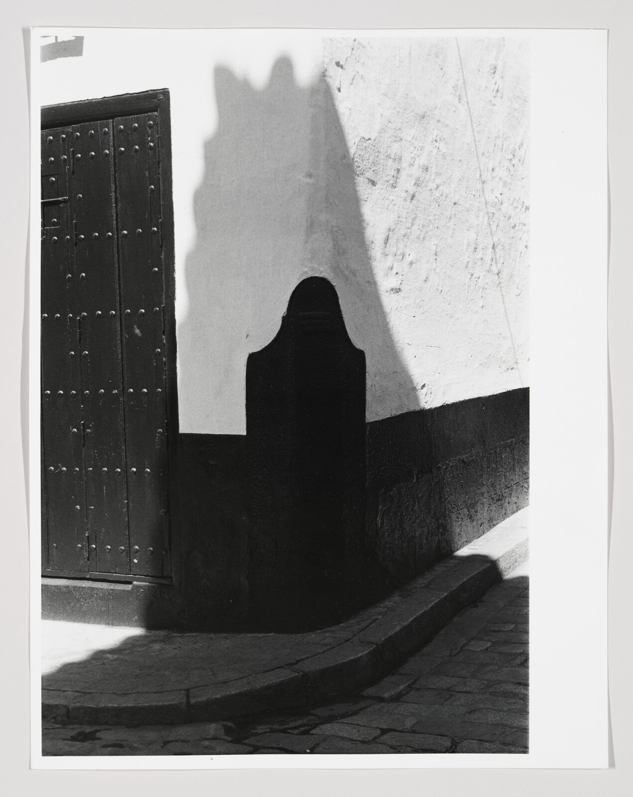 A dark doorway and curved curb cast a strong shadow on a white plaster wall.