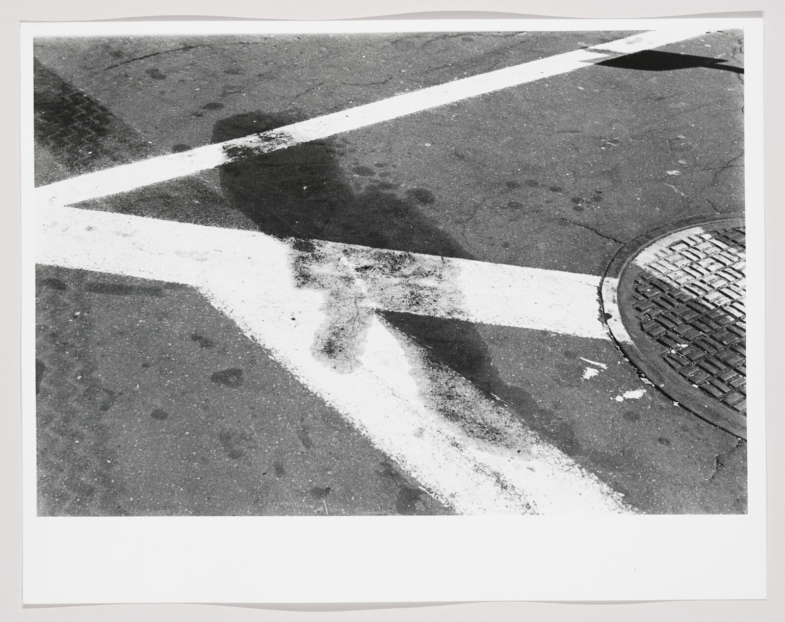 White street lane markings cross a wet oil stain near a round metal manhole cover.