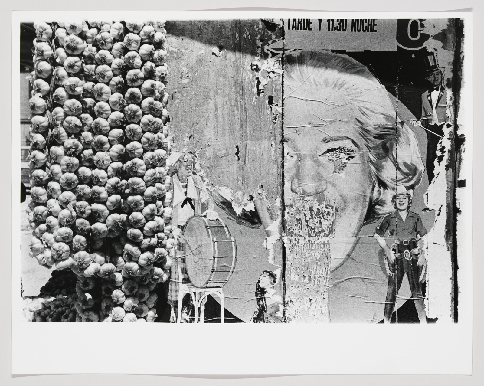 Peeling advertising posters reveal a large woman's face beside hanging bulbs of garlic.