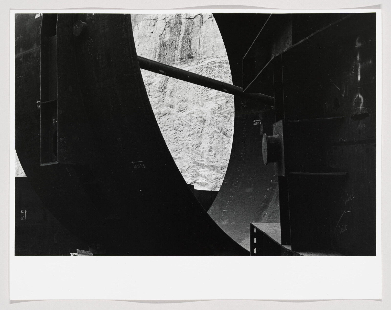 Large curved steel structure frames a rocky cliff through a circular opening.