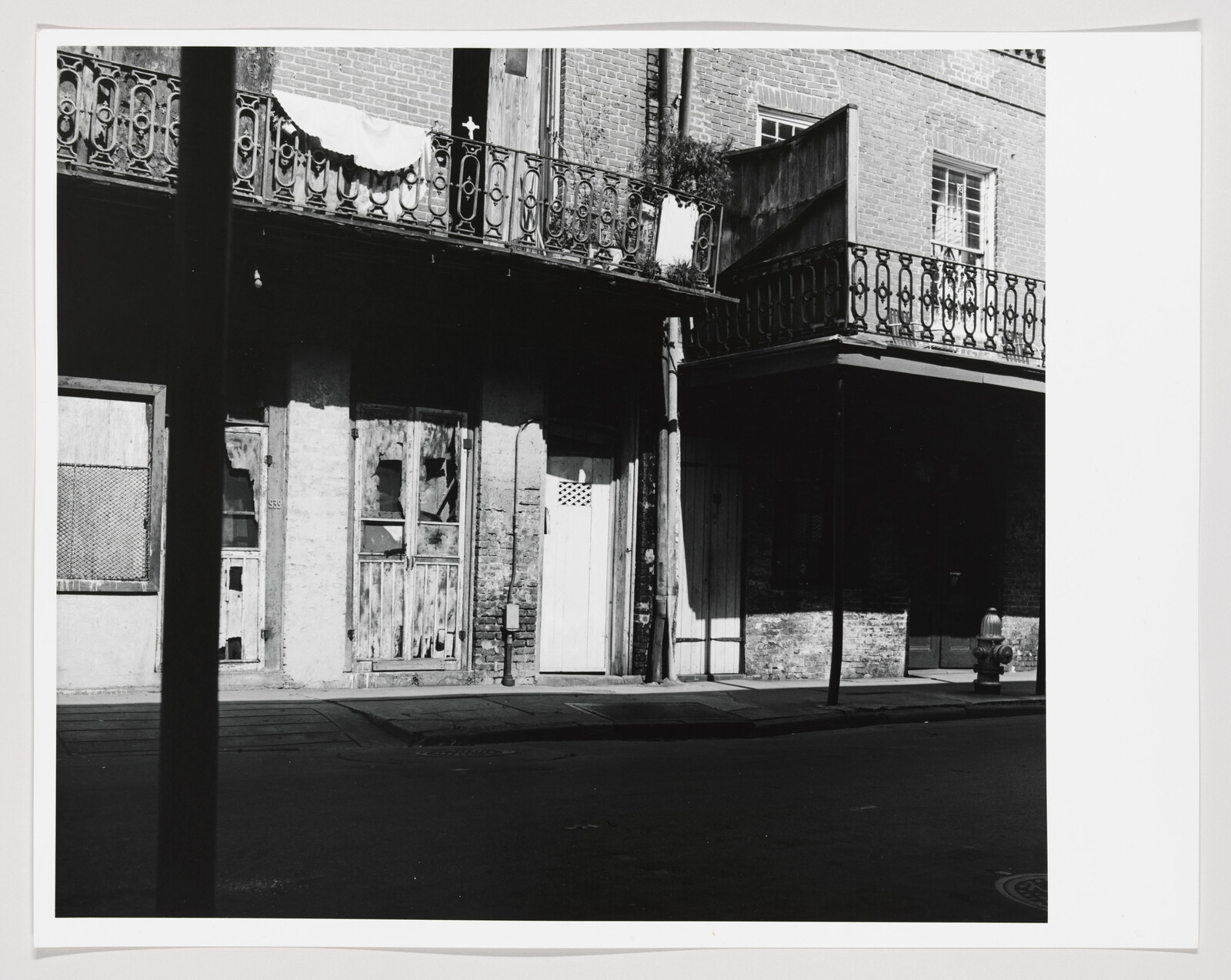 Worn brick storefront with ornate wrought-iron balconies and boarded doors along a quiet street.