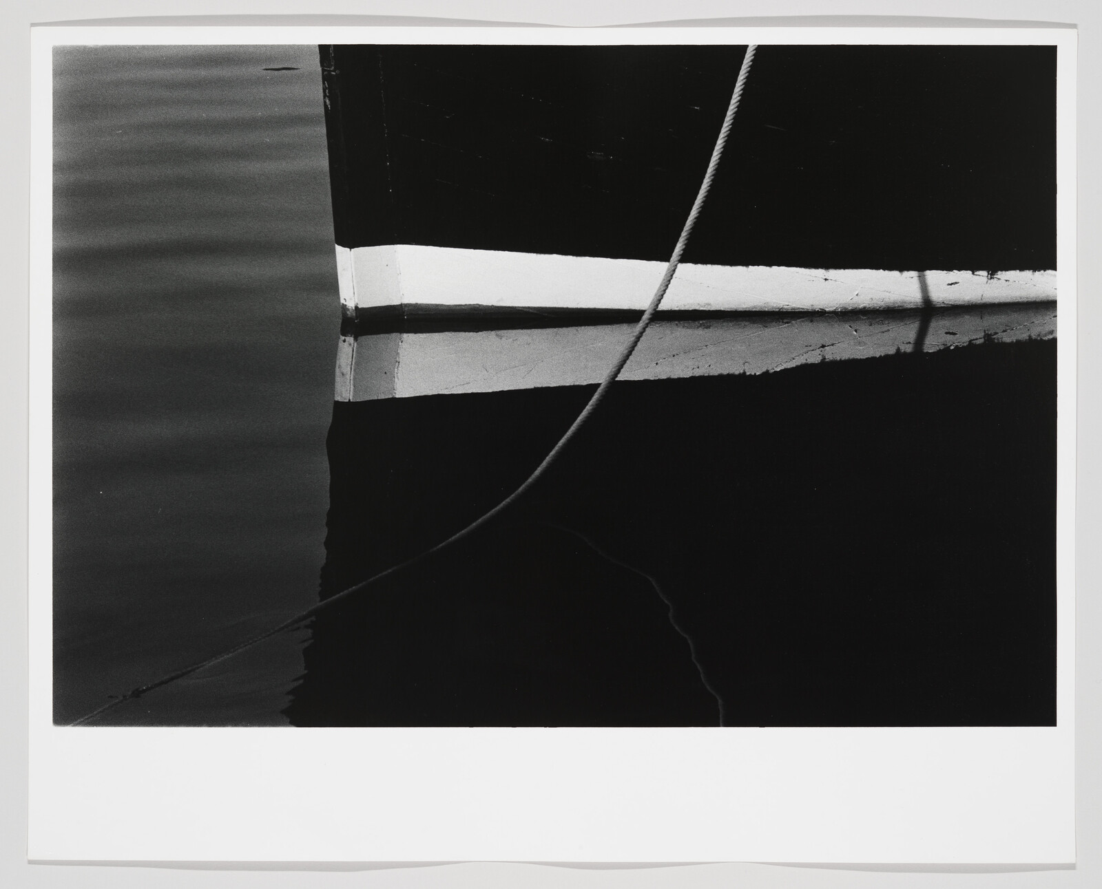 Boat hull with a white waterline reflected in dark water and a rope crossing diagonally.