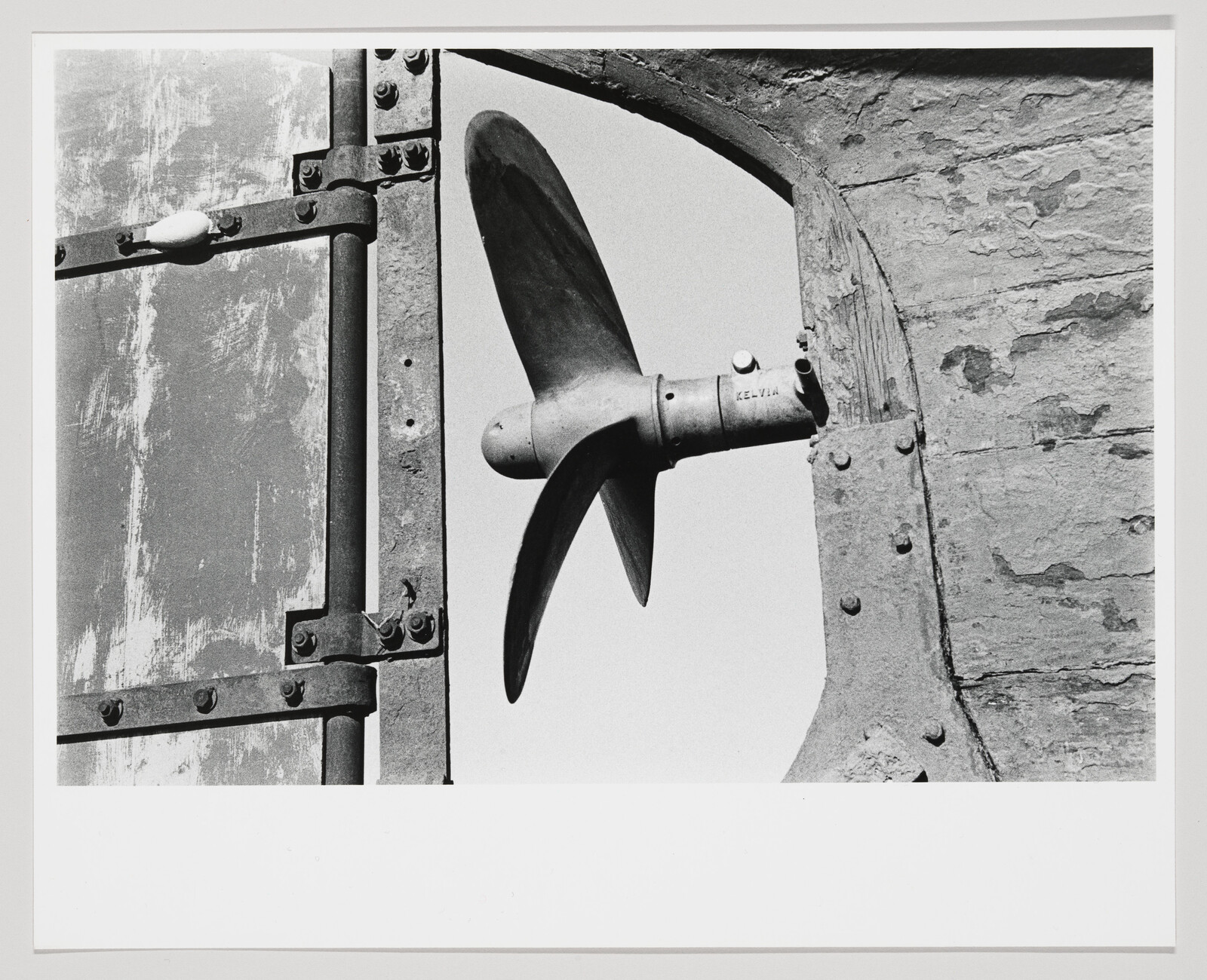 A metal ship propeller blade is mounted through a weathered metal and wooden gate opening.