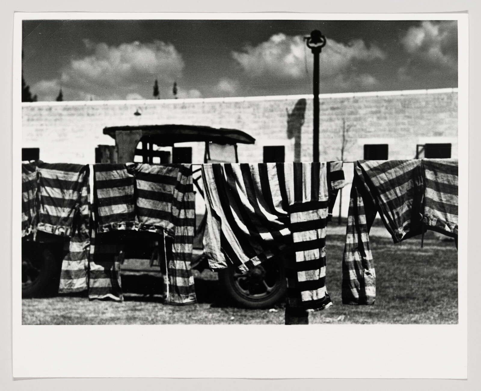 Striped shirts and pants hang on a clothesline outdoors in front of a truck and building.