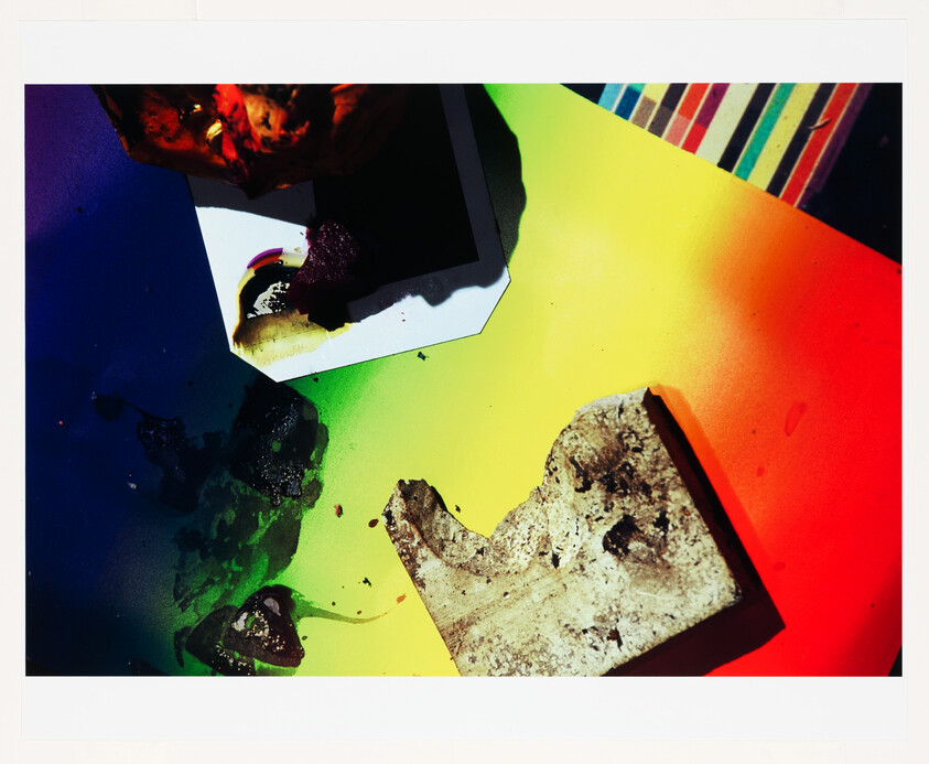 Broken concrete fragment and melted wax pieces scattered on a bright rainbow gradient surface.