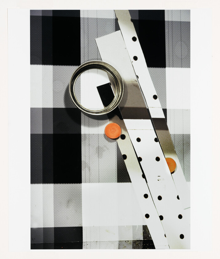 Metal roll of tape and perforated white strips with orange tokens on a checkered surface.