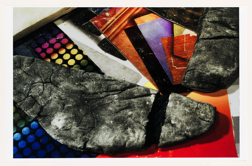 Several cracked pieces of dark modeling clay resting on colorful printed paper.