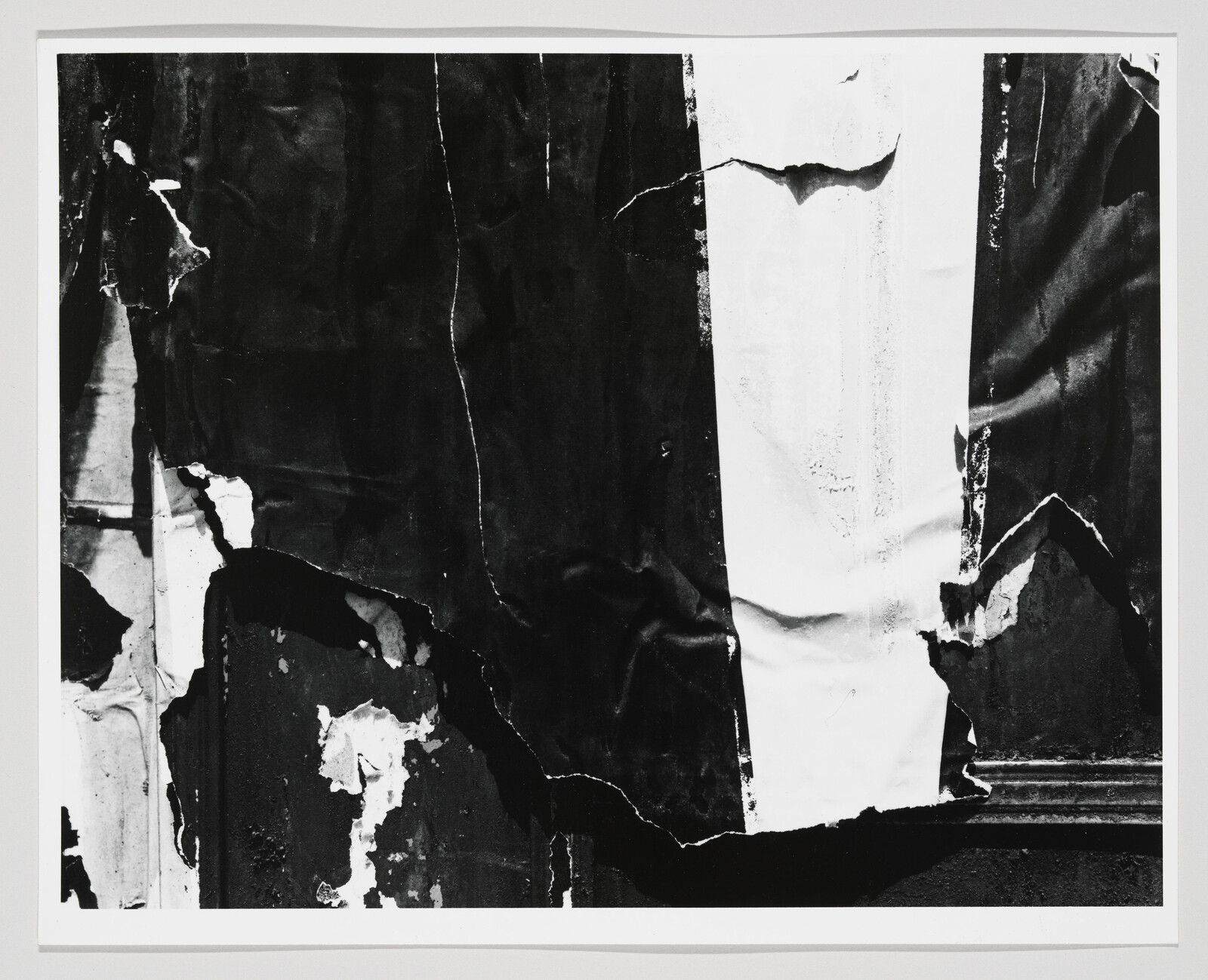 Torn black and white poster layers peel and curl on a weathered wall.