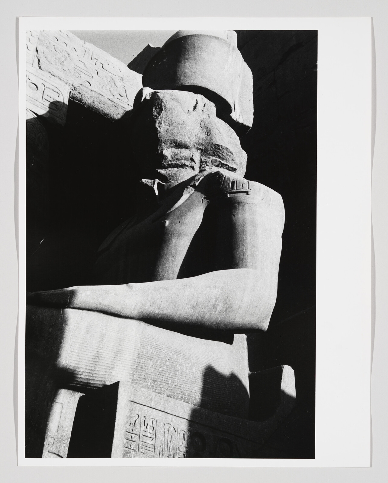 A large ancient Egyptian seated stone statue with a damaged face and visible hieroglyphs.