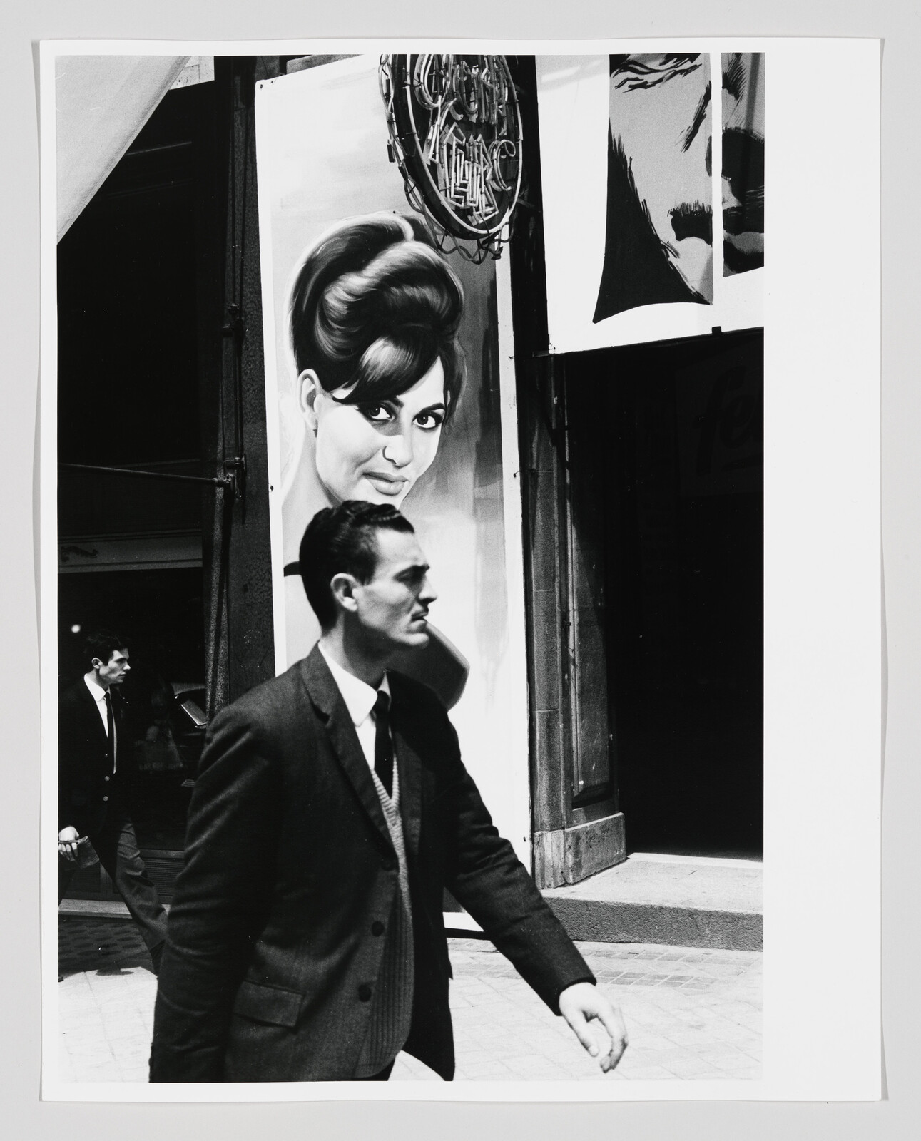 A man in a suit walks past a large poster of a woman's face on a storefront.